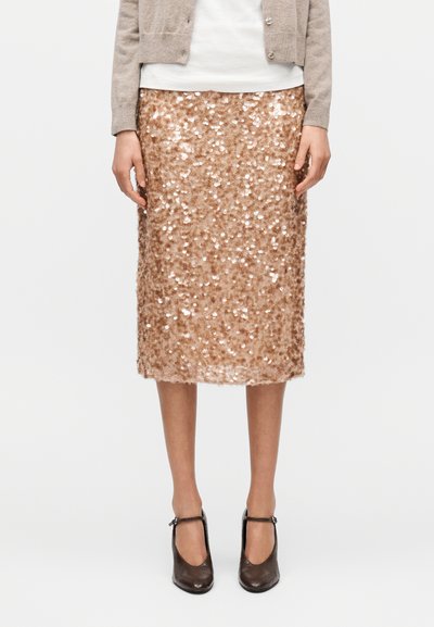 Jupe midi en sequins couleur or rose avec une forme ajustée, une texture brillante et une doublure lisse, associée à des talons foncés avec bride à la cheville.