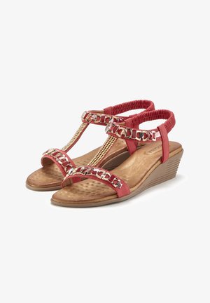 Red sandals with a T-strap design, featuring gold chain accents and a cushioned brown insole. Wedge heel with textured rubber outsole.