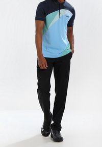 Pikétröja i ljusblått med marinblå krage, med geometriska mönster i teal och beige. Svarta byxor och svarta skor fulländar outfiten.