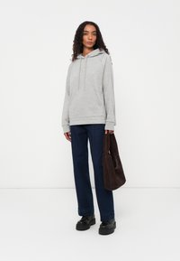 Grijze hoodie met een kangoeroezak en een trekkoord, gecombineerd met donkerblauwe rechte spijkerbroeken. Model houdt een bruine suède tas vast en draagt zwarte schoenen.