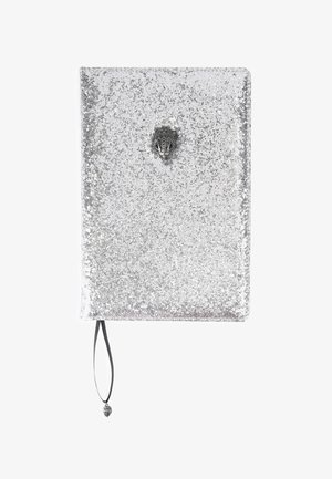 Notitieboek bedekt met zilveren glitters, met een metalen schelpenklem en een zwart lint als bladwijzer, eindigend in een schelpbedel.