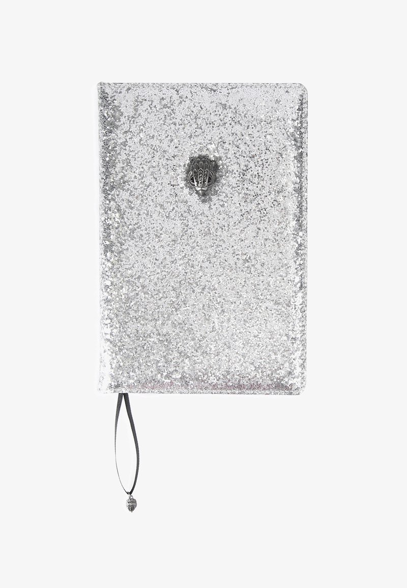 Carnet recouvert de paillettes argentées avec une fermeture en métal en forme de coquillage et un marque-page en ruban noir terminé par un charm en forme de coquillage.