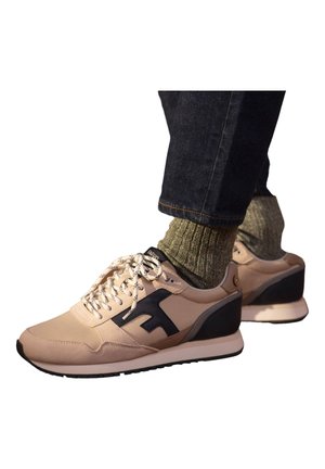 Baskets beiges avec des accents foncés, dotées de lacets, d'une surface texturée et d'un design de talon contrastant. Portées avec des chaussettes vertes et un jean foncé.