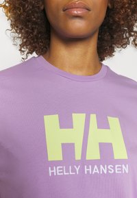 Camiseta de algodón morada con gran logo amarillo "HH" y texto blanco "HELLO HANSEN"; cuello redondo y mangas cortas. Textura suave.