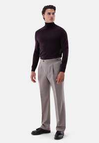 Dunkellila Rollkragenpullover, hellgraue plissierte Hose mit Knopfakzenten und schwarze Lederschuhe. Einfaches, strukturiertes Design.