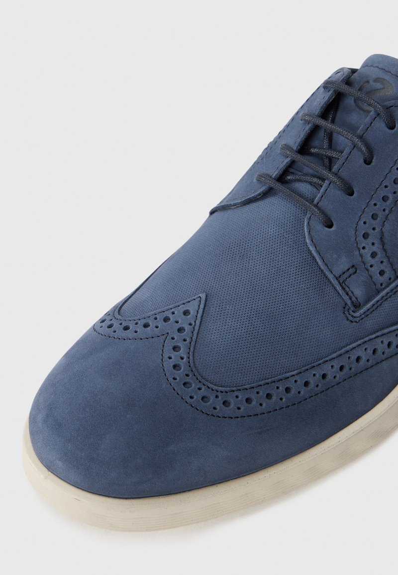 Granatowe zamszowe i siateczkowe sneakersy z perforowanymi detalami w stylu brogu, płaskimi sznurówkami i jasną gumową podeszwą.