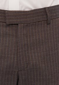 Prunad triibulised püksid, millel on sile tekstuur, lame eesmine osa, nööbikinnitus ja vööde jaoks silmused. Kangas sisaldab peeneid mitmevärvilisi niite.