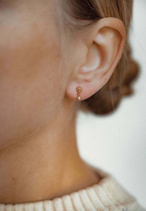 Goldene Steckerohrringe mit floralem Design, kleinen runden Akzenten und einem einzelnen klaren Stein, getragen am Ohr eines Modells.