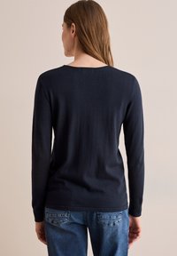 Navyblauw langesleeve trui met een ronde hals en ribgebreide manchetten, gecombineerd met lichtblauwe jeans met gestikte zakdetails.
