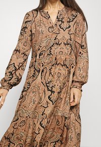 Vestido de manga larga, con escote en V y estampado de paisley, que presenta tonos de durazno y negro, con puños fruncidos y una falda en capas.