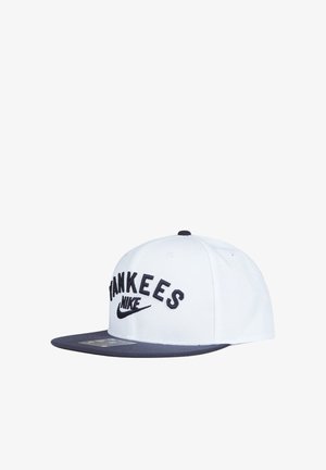 Cappellino da baseball bianco e blu navy con scritta "YANKEES" e logo Nike ricamati in nero sul davanti, visiera piatta, mostrato su sfondo bianco.