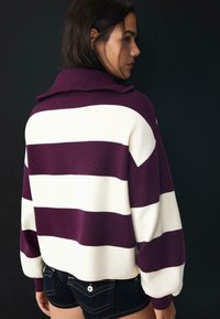 Pull-over rayé violet et blanc avec un col rabattu et des manches ballons, fabriqué dans un matériau tricoté doux.