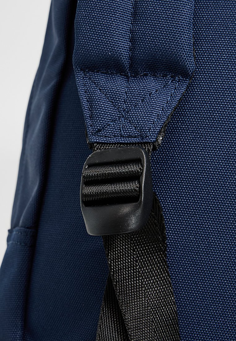 Zaino blu navy in tessuto di nylon texturizzato con fibbia in plastica nera. Sono visibili spallacci imbottiti e cuciture rinforzate.