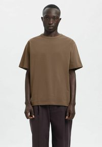 Pruun puuvillane t-särk, lõdvalt istuv, lühikeste varrukatega ja ümmarguse kaelusega. Lihtne disain, sile tekstuur, nähtavaid mustreid ega aktsente puudub.