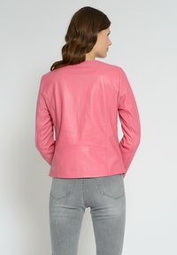 Rosa læderjakke med tætsiddende design og lange ærmer, der har syede detaljer og en glat tekstur. Kombinationen er med grå jeans.