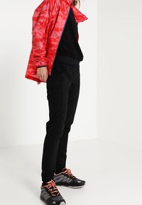 Röd kamouflagejacka med dragkedja, svart sweatshirt, svarta tapered byxor och svarta sneakers med rosa accenter. Slätt, lättviktigt material.