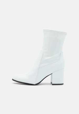 Witte enkellaarsjes van glanzend materiaal, met een puntige neus, blokhak en een nauwsluitend, transparant bovenwerk.