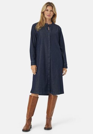 Jeanshemdkleid, dunkelblau, Knopfleiste vorne, lange Ärmel, lockerer Schnitt, knielang, kombiniert mit braunen Stiefeln bis zum Knie.