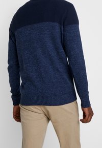 Navyfarbener und blauer gestrickter Pullover mit strukturiertem Design, langen Ärmeln, gerippten Bündchen und Saum. Getragen über hellen Hosen.