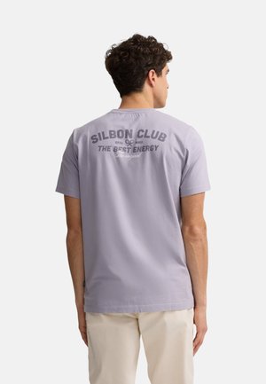 Camiseta de algodón lila con cuello redondo, mangas cortas y gráfico en la parte posterior con el texto: "SILBON CLUB EST. MIX THE BEST ENERGY" en gris oscuro.