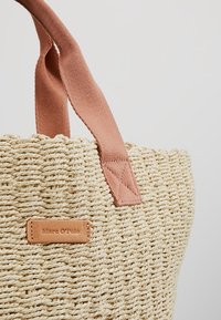 Sac fourre-tout en paille tissée avec un corps beige texturé, deux poignées en coton rose et une petite étiquette en cuir marron avec le nom de la marque, Marc O'Polo.