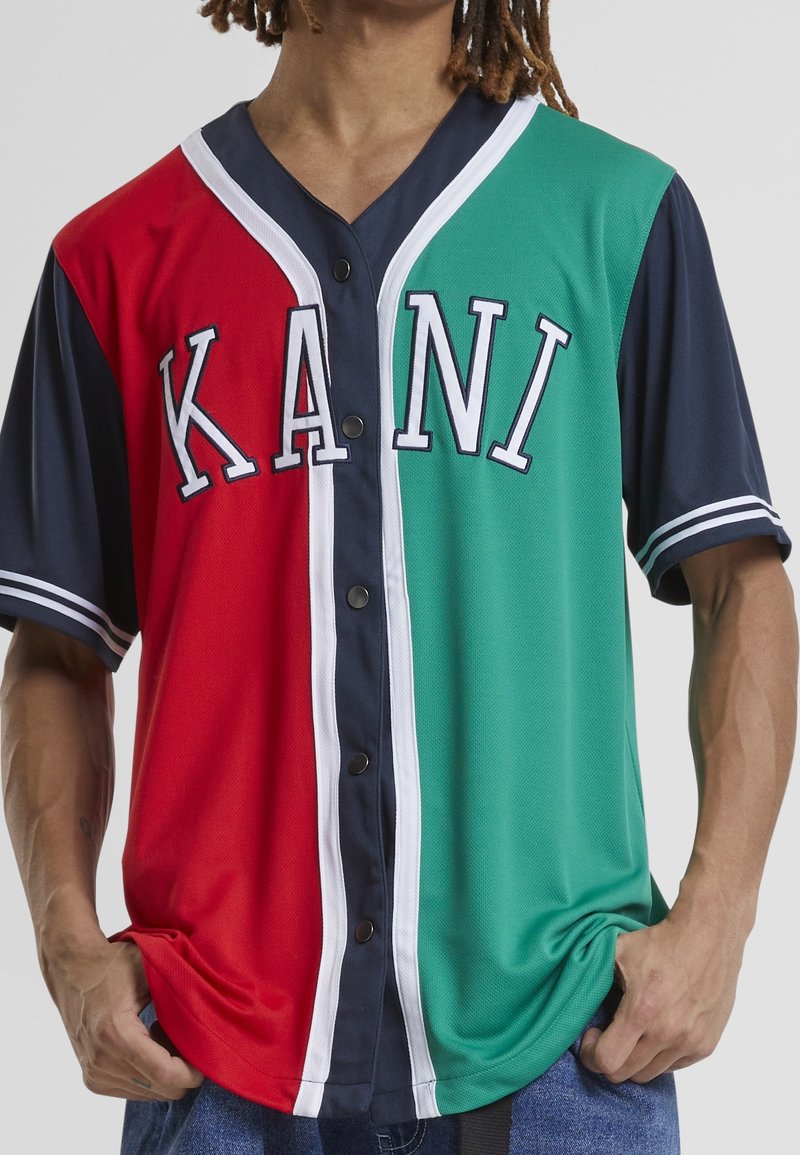 Maillot bicolore avec sections rouges, vertes et bleu marine ; accents blancs ; grand texte "KANI" ; manches courtes ; fermeture à boutons.