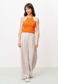 Oranje gebreide haltertop en brede gestreepte broek in pastelkleuren. Platte schoenen met een eenvoudig ontwerp complementeren de outfit.
