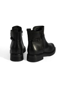 Bottes de cheville en cuir noir avec une texture lisse, des fermetures éclair sur le côté et un petit talon carré. Présente une courte sangle avec un détail de boucle en métal.