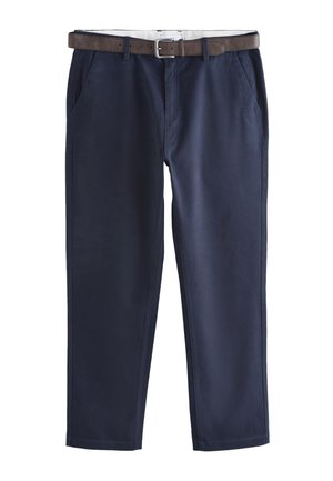 Tył osoby noszącej ciemnogranatowe spodnie z tylne kieszenie z patkami i brązowy skórzany pasek, w połączeniu z białą koszulą.