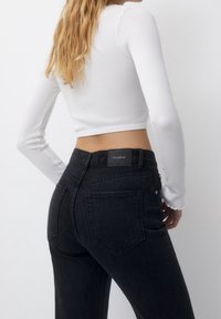 Vaqueros de mezclilla negra de cintura alta con una silueta ajustada, que incluyen bolsillos traseros y una etiqueta negra en la cinturilla. Top blanco de manga larga con textura en relieve.