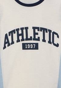Weißes Baumwoll-T-Shirt mit marineblauem „ATHLETIC“-Text und „1997“ in der Mitte. Runder Halsausschnitt mit kontrastierendem marineblauem Rand.