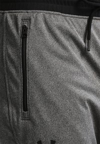 Graue Sportshorts aus strukturiertem Stoff, mit elastischem Bund, Kordelzug und einer seitlichen Reißverschlusstasche mit schwarzen Akzenten.