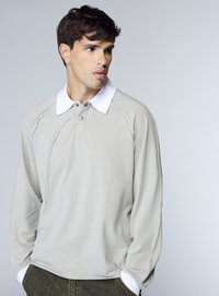 Polo a maniche lunghe grigio chiaro con colletto bianco, caratterizzata da una pattina con bottoni e dettagli di cuciture a contrasto. Tessuto morbido al tatto.