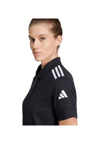 Zwarte poloshirt met een kraag, voorzien van drie witte strepen op de schouder en een wit logo op de mouw. Gedetailleerde textuurstof.