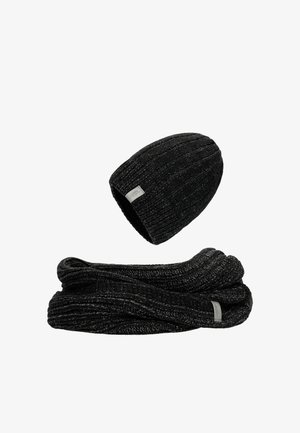 Zwarte gebreide beanie met ribbelpatroon en klein label, gecombineerd met een bijpassende ribbel sjaal, beide gemaakt van zachte, gestructureerde stof.