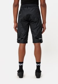 Pantaloni sportivi neri con una finitura leggera e lucida; cintura elastica; dettagli riflettenti; e polsini con chiusure in Velcro.