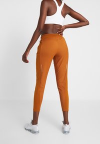 Oranger Sport-Leggings mit schlankem Schnitt, elastischem Bund und Reißverschlusstaschen. Kombiniert mit einem weißen Sport-BH und weißen Turnschuhen.