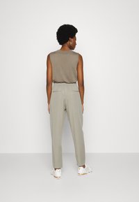Top bege ligeiramente texturizado sem mangas combinado com calças cinza claro ajustadas. Apresenta uma cintura elástica e um design minimalista. Ténis brancos.
