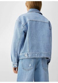 Světle modrá džínová bunda s volným střihem, velkým límcem a manžetami na knoflíky. Má viditelné švy a lehce zkrácenou délku.