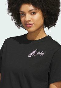 Čierne bavlnené tričko s ružovou vyšitou logom na ľavej strane hrude, okrúhlym výstrihom a krátkymi rukávmi.