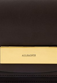 Čierna kožená kabelka s hladkým povrchom, zlatým kovovým kovaním s vyrazeným nápisom "ALLSAINTS" a elegantnými švami.