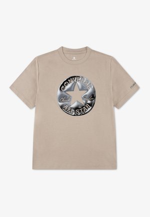 Beżowy t-shirt z krótkim rękawem z dużym metalicznym srebrnym logo Converse All Star i tekstem "Chuck Taylor" na przodzie.