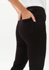 Jeans negros hechos de algodón elástico, con un corte ajustado, bolsillos traseros con solapas angulares y una textura suave.