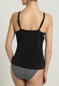 Top de banho preto com alças ajustáveis, textura lisa e costuras planas. Combinado com um fundo de bikini preto e branco padrão com formas de diamante.