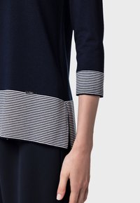 Maglione blu navy con maniche tre quarti e orlo a strisce. Tessuto morbido, con un piccolo logo vicino all'orlo e una fessura laterale.