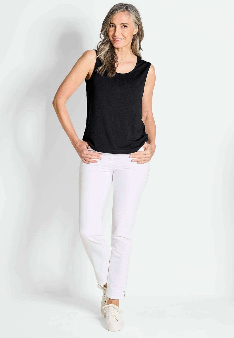 Schwarzes ärmelloses Oberteil mit rundem Halsausschnitt, kombiniert mit weißen enganliegenden Hosen und cremefarbenen Sneakern. Das Outfit hat ein lässiges Design und eine glatte Textur.