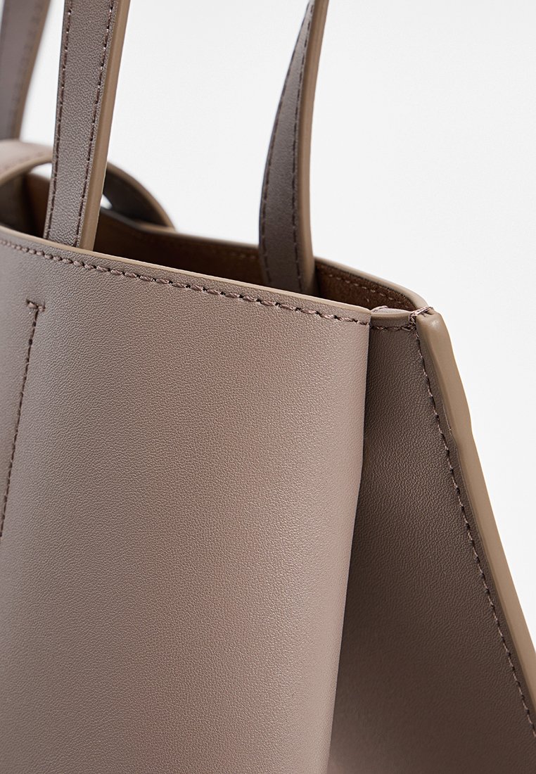 Graue Kunstleder-Totetasche mit strukturierten Seiten und glatter Oberfläche, ausgestattet mit zwei flachen Tragegriffen und sauberem Steppdetail an den Kanten.