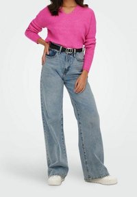 Rosa Strickpullover mit V-Ausschnitt, kombiniert mit hoch taillierten, hellblauen, weit geschnittenen Jeans und einem schwarzen Gürtel mit einer silbernen runden Schnalle.