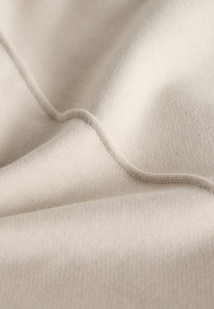 Beżowa dzianina o gładkiej fakturze, ukazująca miękkie fałdy i subtelne szwy. Powierzchnia wydaje się równa i spójna, podkreślając jej lekkość.