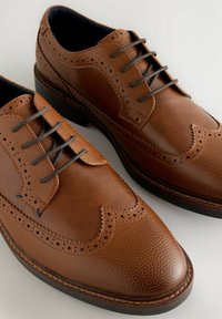 Zapatos de vestir de cuero marrón con detalles de brogue perforados, punteras redondas y cordones oscuros. Parte superior texturizada con acentos suaves.